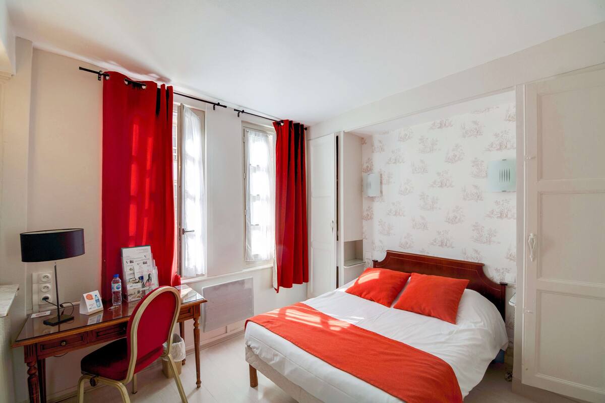 Ein Hotelzimmer mit Bett, Schreibtisch, Stuhl, Heizkörper und einem Fenster mit Vorhängen.