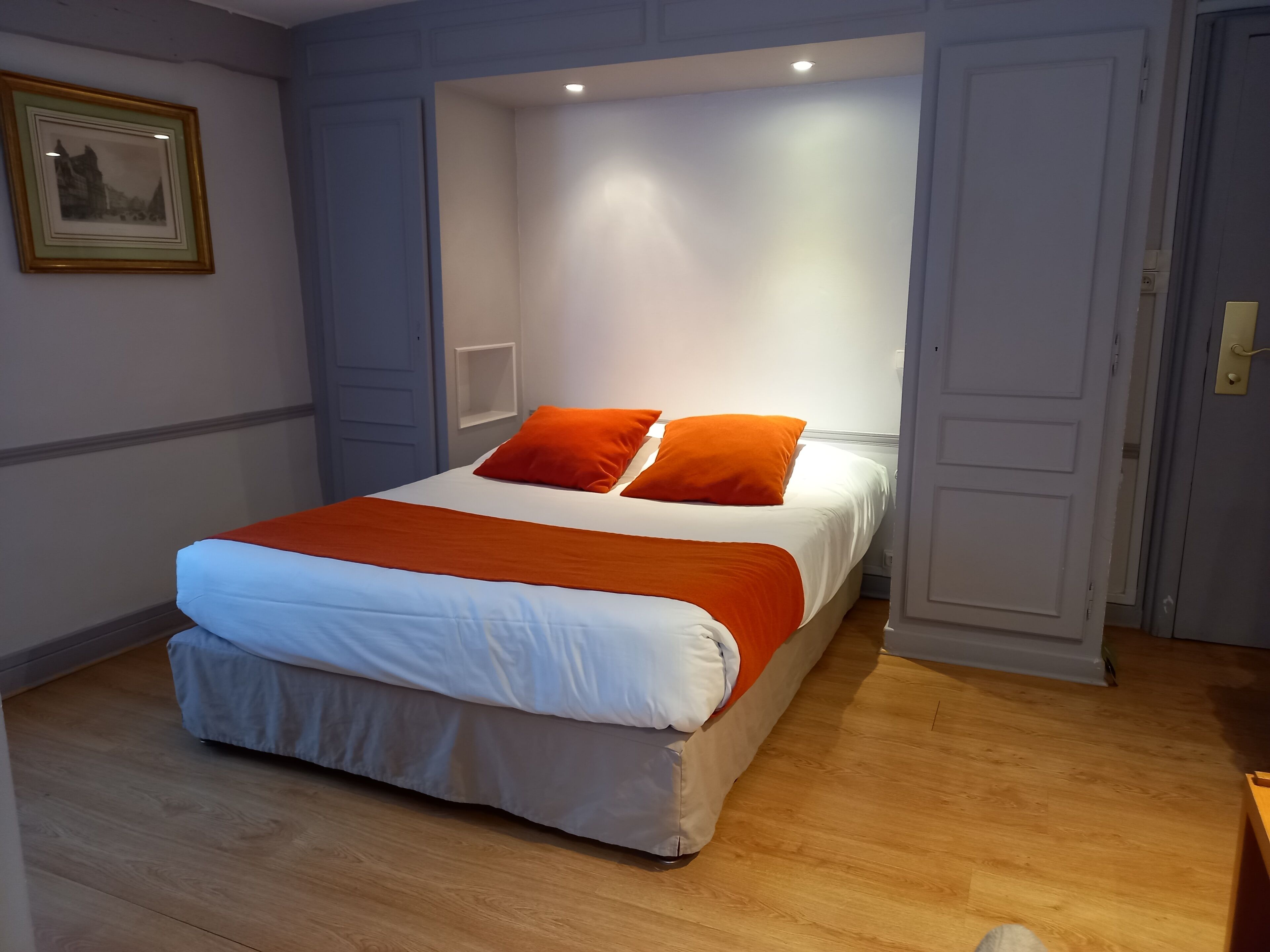 A bedroom with a bed, orange pillows, and a white bedspread.