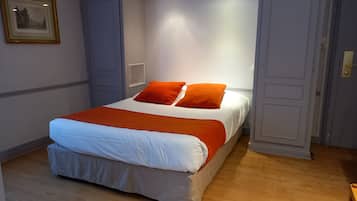 A bedroom with a bed, orange pillows, and a white bedspread.