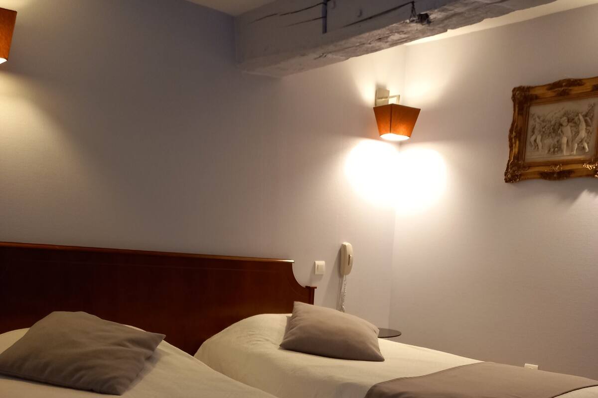 Ein Hotelzimmer mit zwei Betten, jeweils mit Kopfteil, Nachttisch und Lampe.