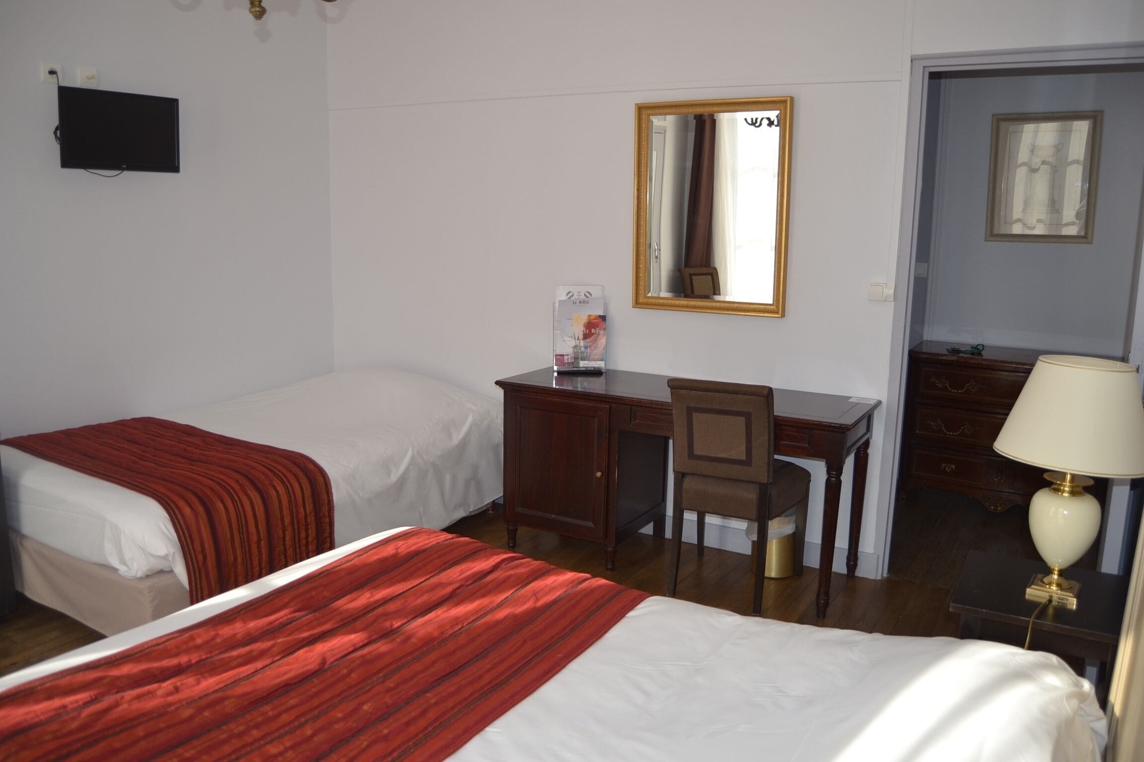 Habitación de hotel con dos camas, un escritorio, una silla, un televisor, un espejo y una lámpara.