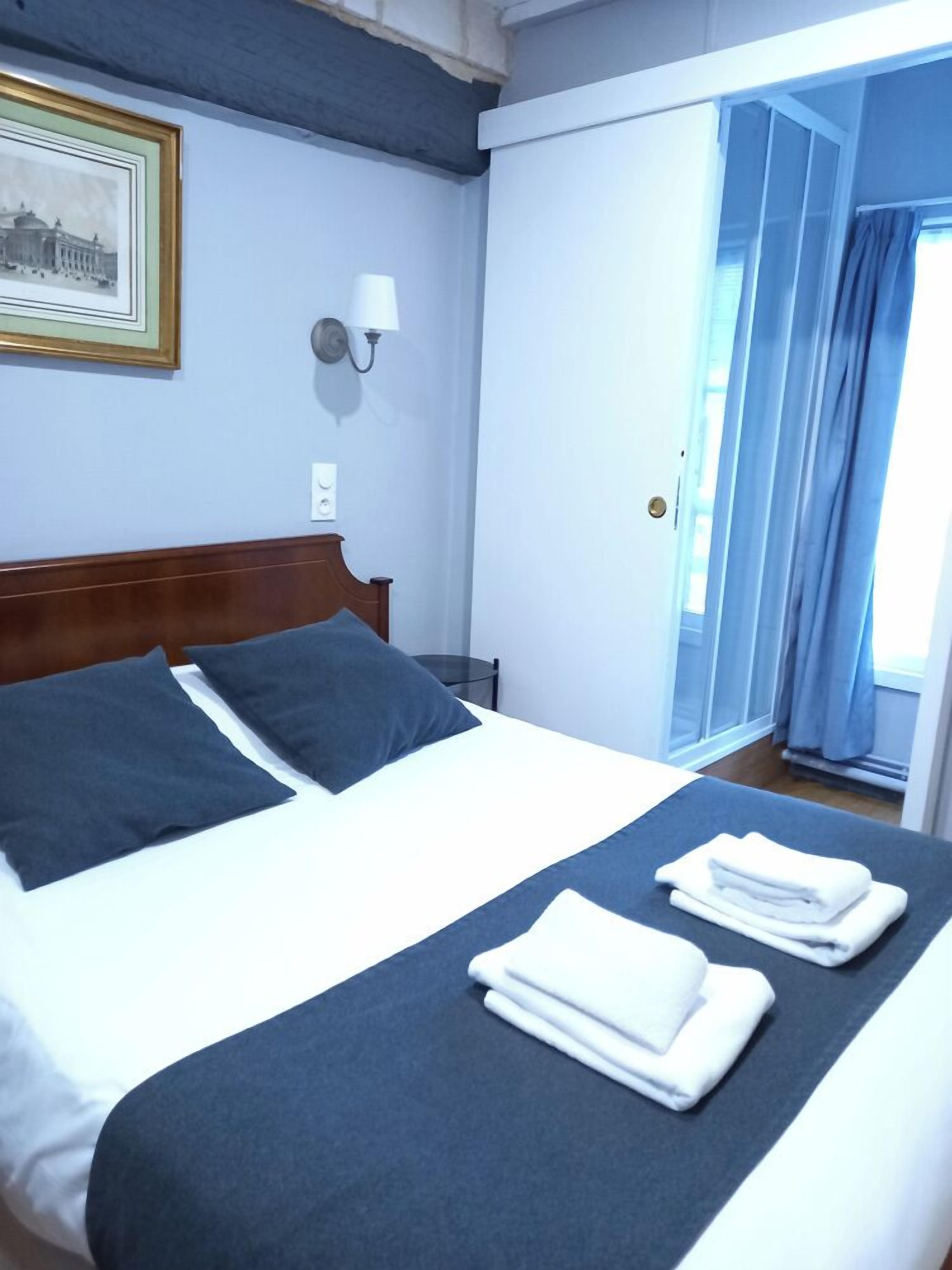 Una camera d'albergo con un letto, cuscini, un comodino, una lampada a parete e un quadro incorniciato.