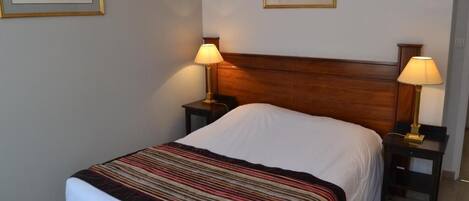 A neatly made bed with a striped blanket, two bedside lamps, and two framed pictures on the wall.