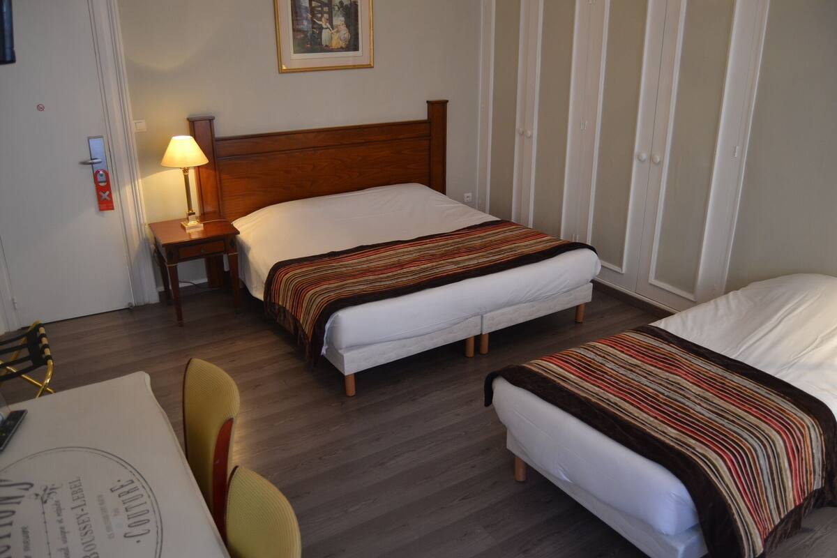 Ein Hotelzimmer mit zwei Einzelbetten, einem Holzkopfende, einem Nachttisch mit Lampe, einem Sessel und einem Tisch mit Speisekarte.