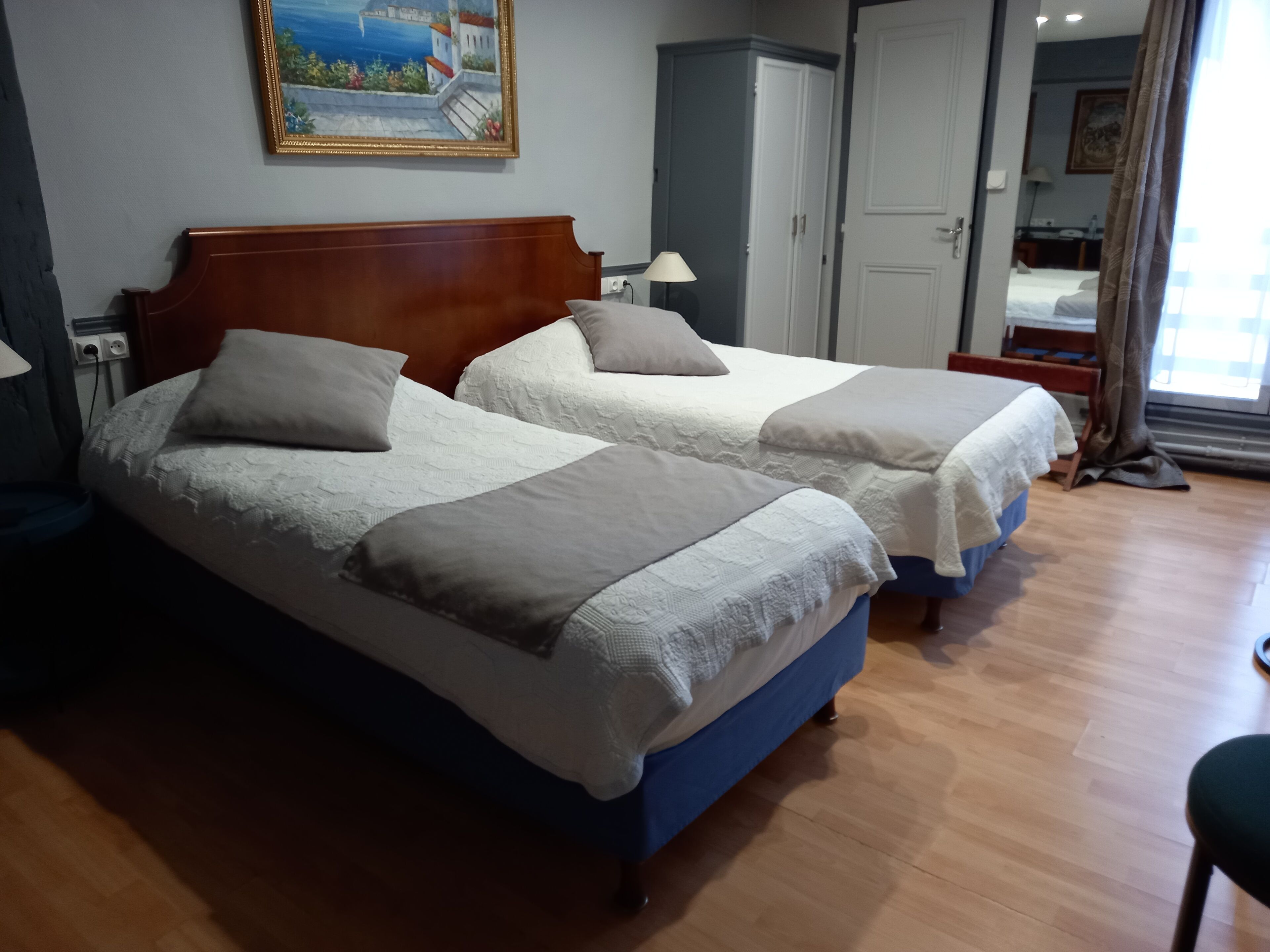 Habitación de hotel con dos camas, un armario, un cuadro en la pared y vistas al exterior.