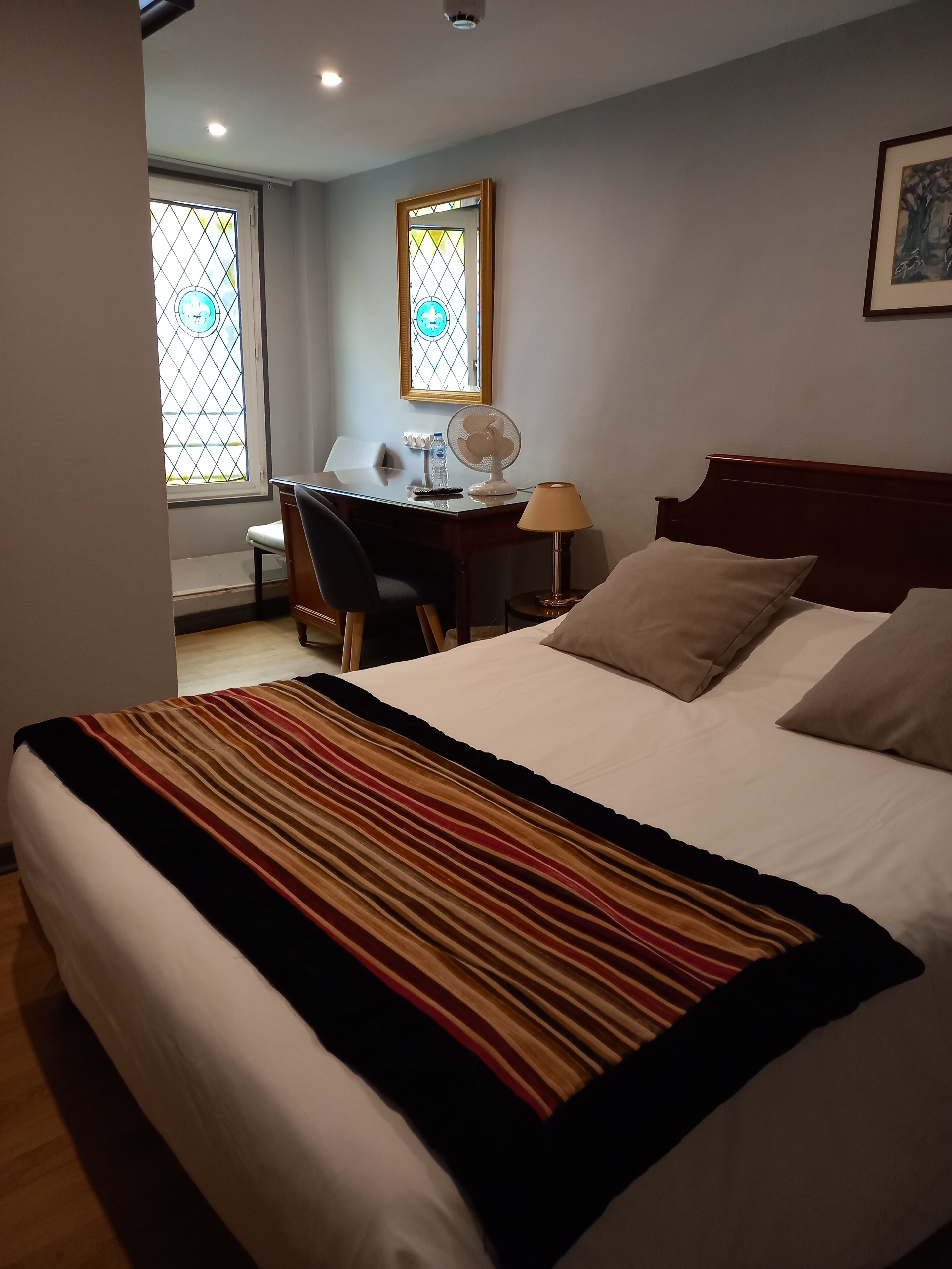 A hotel room with a bed, a desk, a chair, a lamp, and a window with a view.