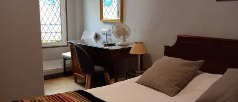 A hotel room with a bed, a desk, a chair, a lamp, and a window with a view.