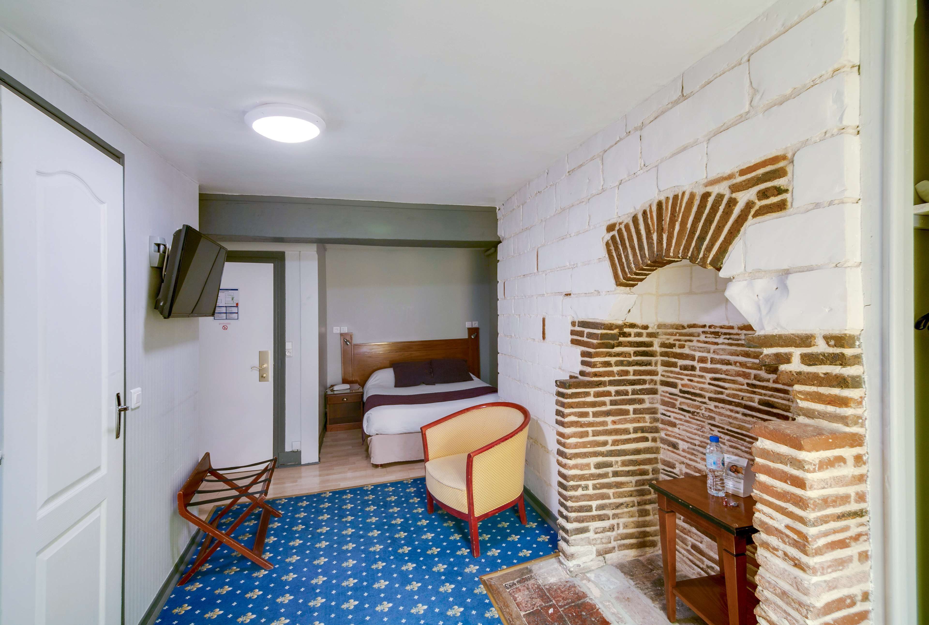 A room with a bed, a chair, a small table, and a brick wall.