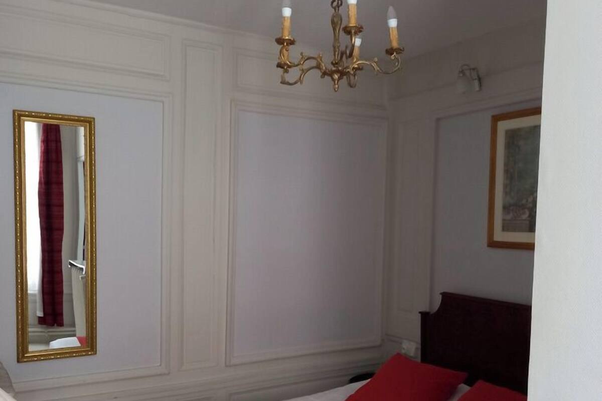 Ein Hotelzimmer mit Bett, Schreibtisch, einer Wasserflasche, einem Spiegel und einer Chandelier.