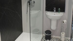 A bathroom with a glass-enclosed shower, a white sink, a black marble-tiled wall, and patterned floor tiles. - Acomb Lodge (Harrogate)
