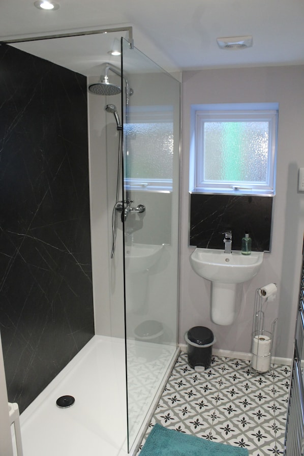 Un baño con ducha envuelta en vidrio, un lavamanos blanco, una pared revestida de mármol negro y baldosas de piso estampadas.