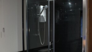 A modern bathroom with a glass-enclosed shower, black tiled walls, and a white toilet. - Acomb Lodge (Harrogate)