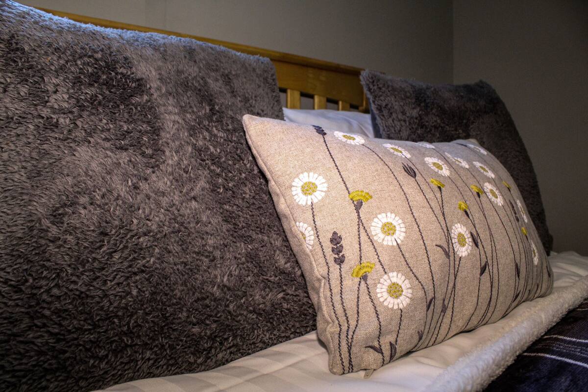A bed with a fluffy grey blanket and a pillow with a floral pattern.