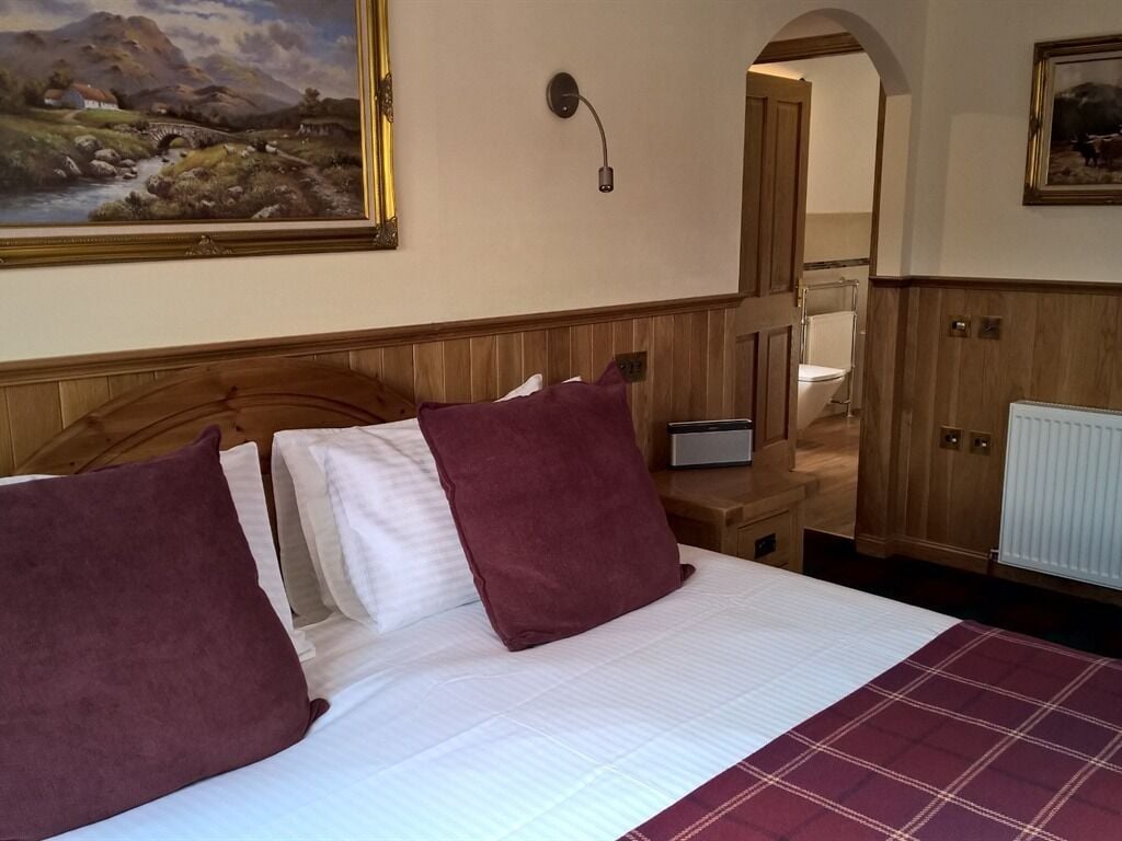 Een hotelkamer met een bed, een schilderij aan de muur, een houten hoofdbord, een nachtkastje met een lamp en uitzicht op de badkamer.