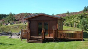 A wooden cabin with a deck, surrounded by a grassy area and hills in the background. - Binnilidh Mhor B&B (Inverness)
