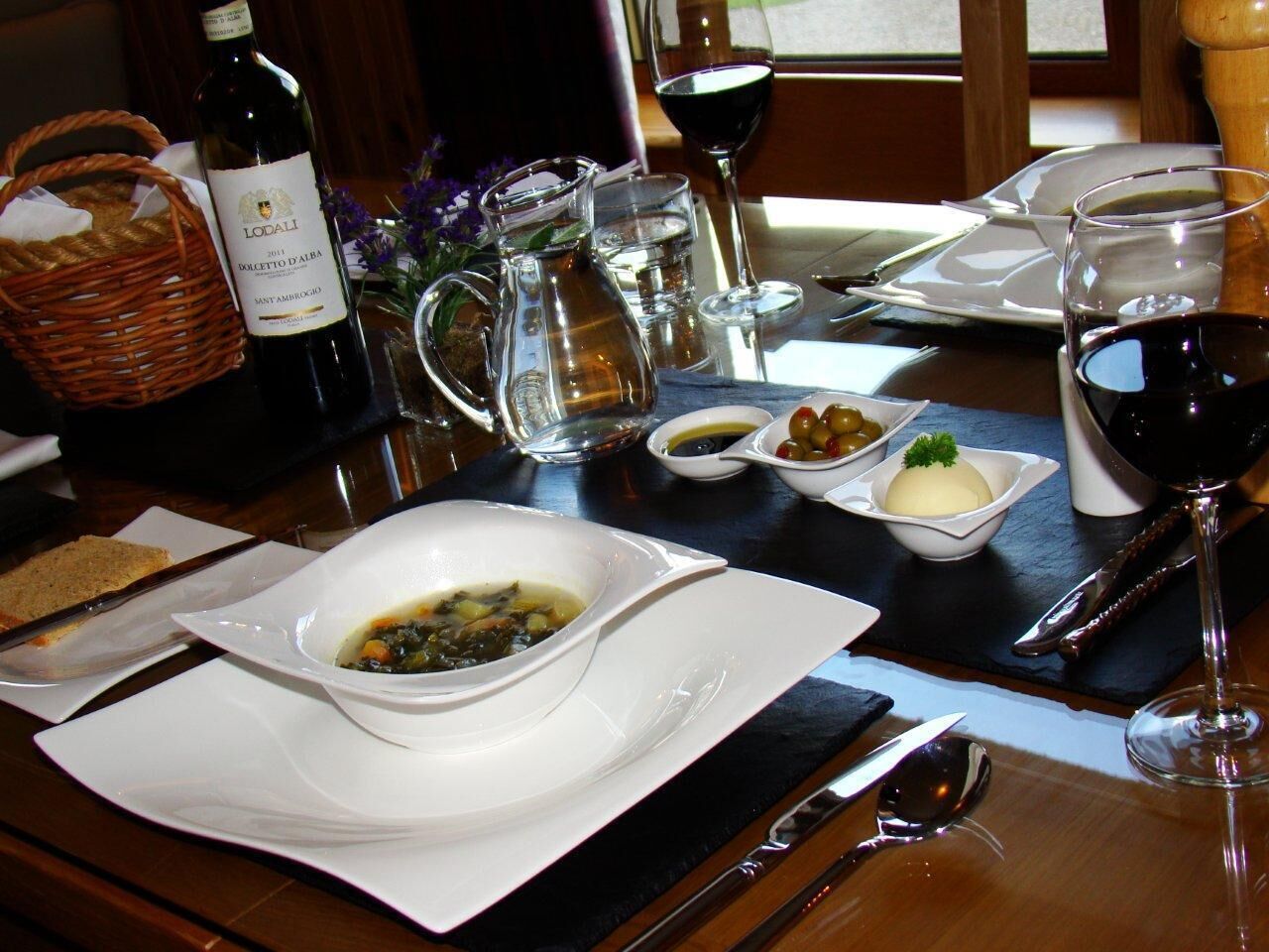 A dining table set with a bottle of wine, a pitcher, glasses, and plates with food.