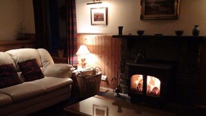 A cozy living room with a sofa, a table, a fireplace, and a lamp. - Binnilidh Mhor B&B (Inverness)
