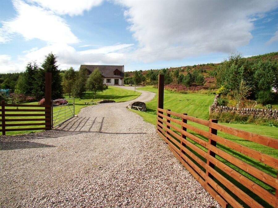 A gravel driveway leading to a house with a wooden fence on one side and a stone wall on the other.