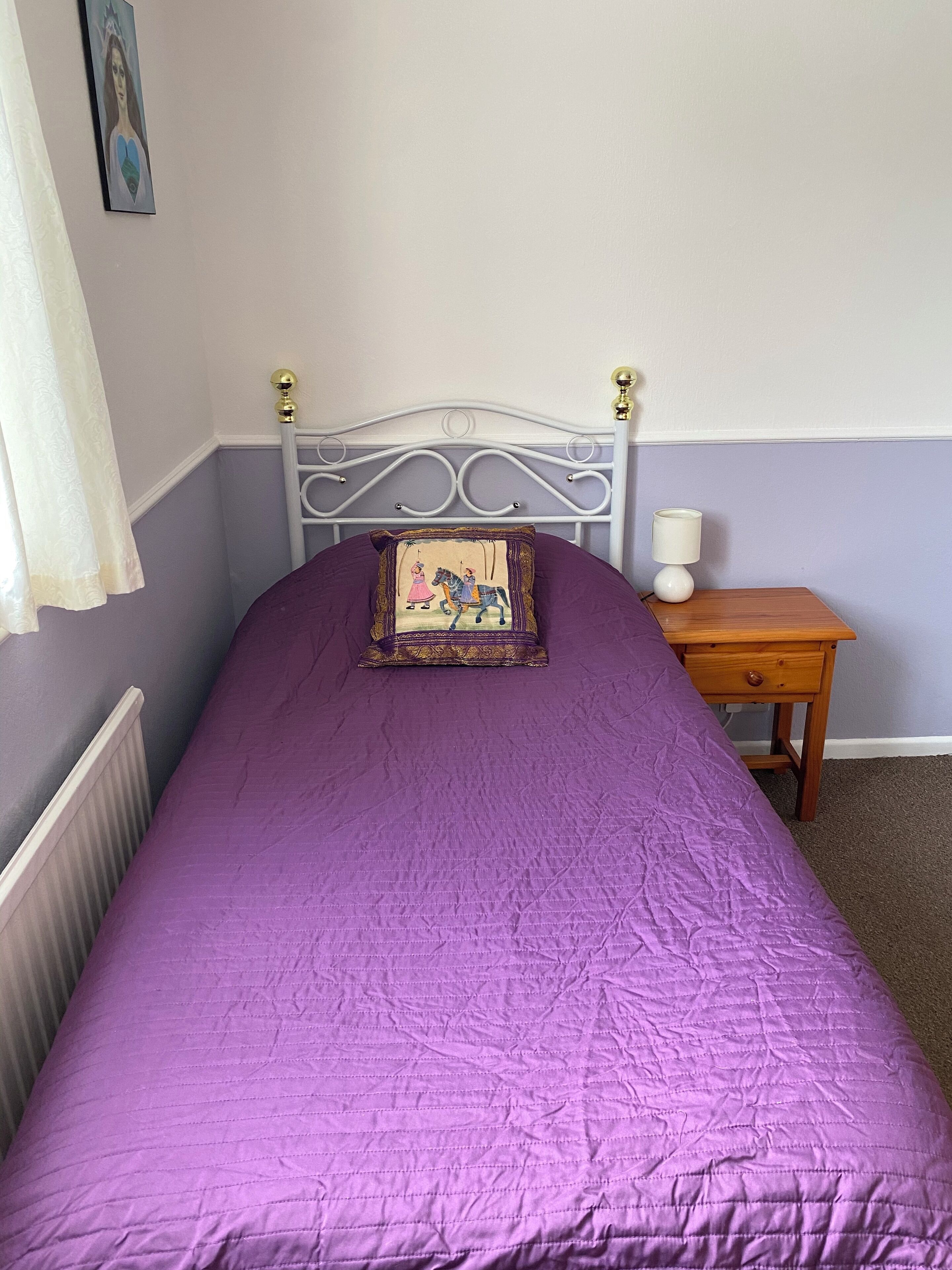 Un dormitorio con cama, mesita de noche, lámpara y un cuadro en la pared.