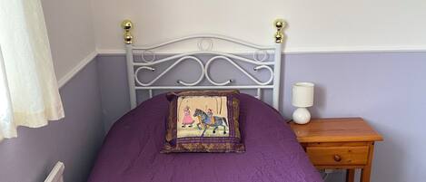Un dormitorio con cama, mesita de noche, lámpara y un cuadro en la pared.