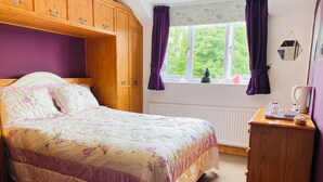 A bedroom with a bed, wooden wardrobe, window with curtains, and a small wooden table with a kettle. - Camelot Retreat (Glastonbury)