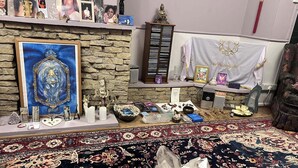 A room with a stone wall, a framed painting, a statue, a white cloth with a golden emblem, and a crystal on a patterned rug. - Camelot Retreat (Glastonbury)