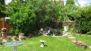 A well-maintained garden with a variety of flowers, a small pond with a statue, and a metal table. - Camelot Retreat (Glastonbury)