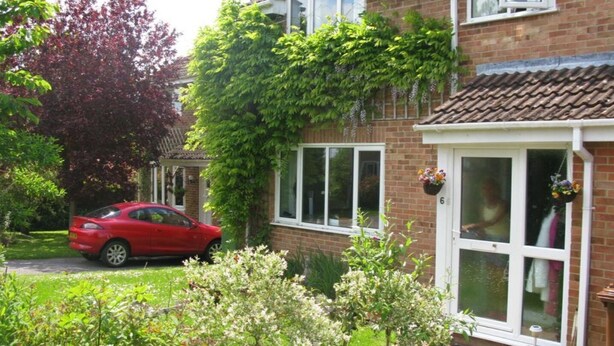 A two-story house with a red car parked in the driveway, surrounded by greenery and a well-maintained garden. - Camelot Retreat (Glastonbury)
