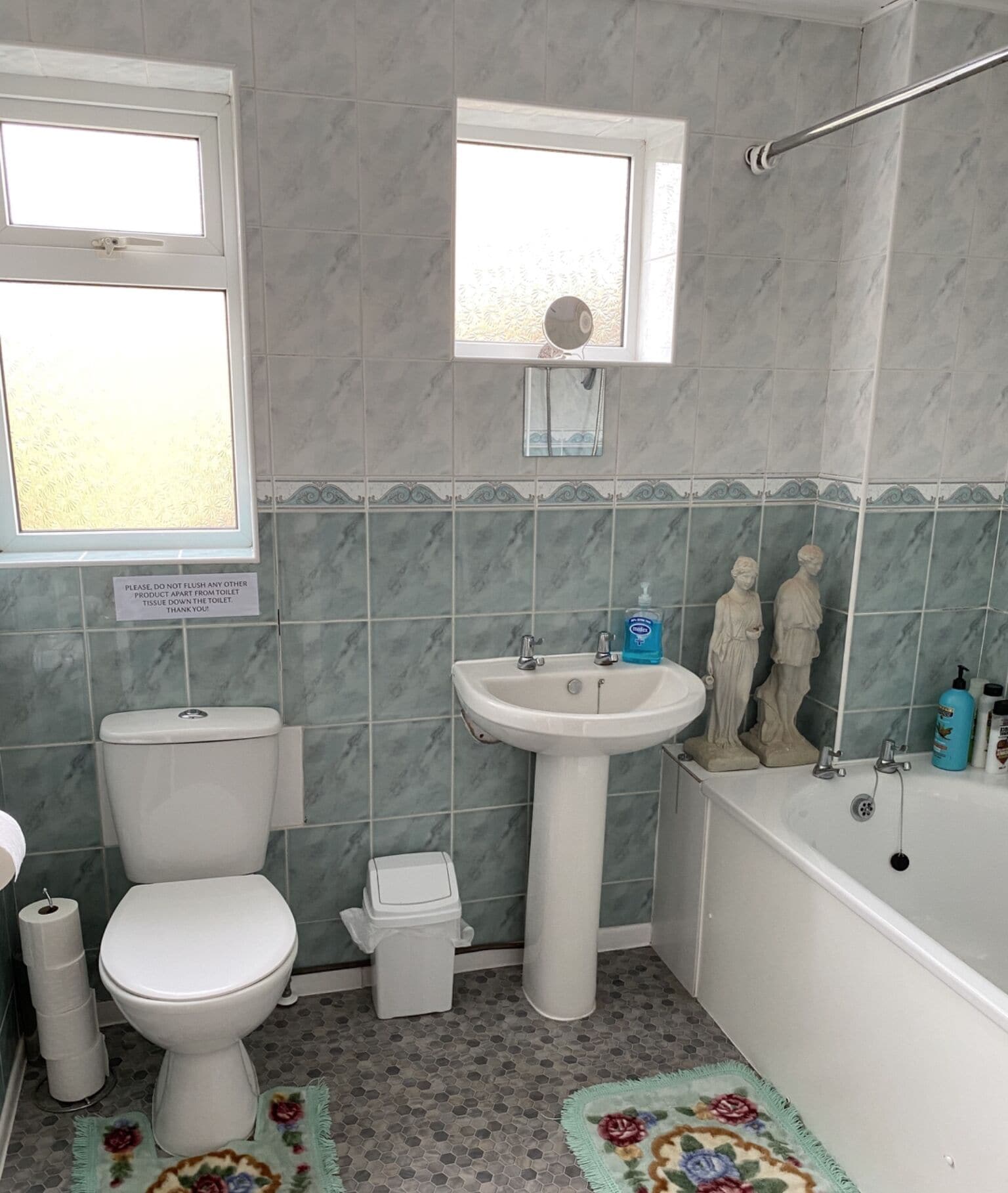 A bathroom with a toilet, sink, and bathtub. There is a sign on the wall and a window above the toilet.