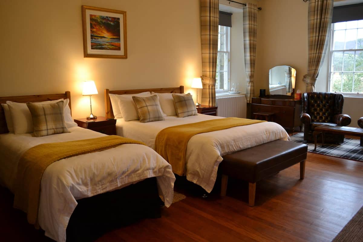 Une chambre d’hôtel avec deux lits, un banc, une commode, une chaise et une fenêtre avec des rideaux.