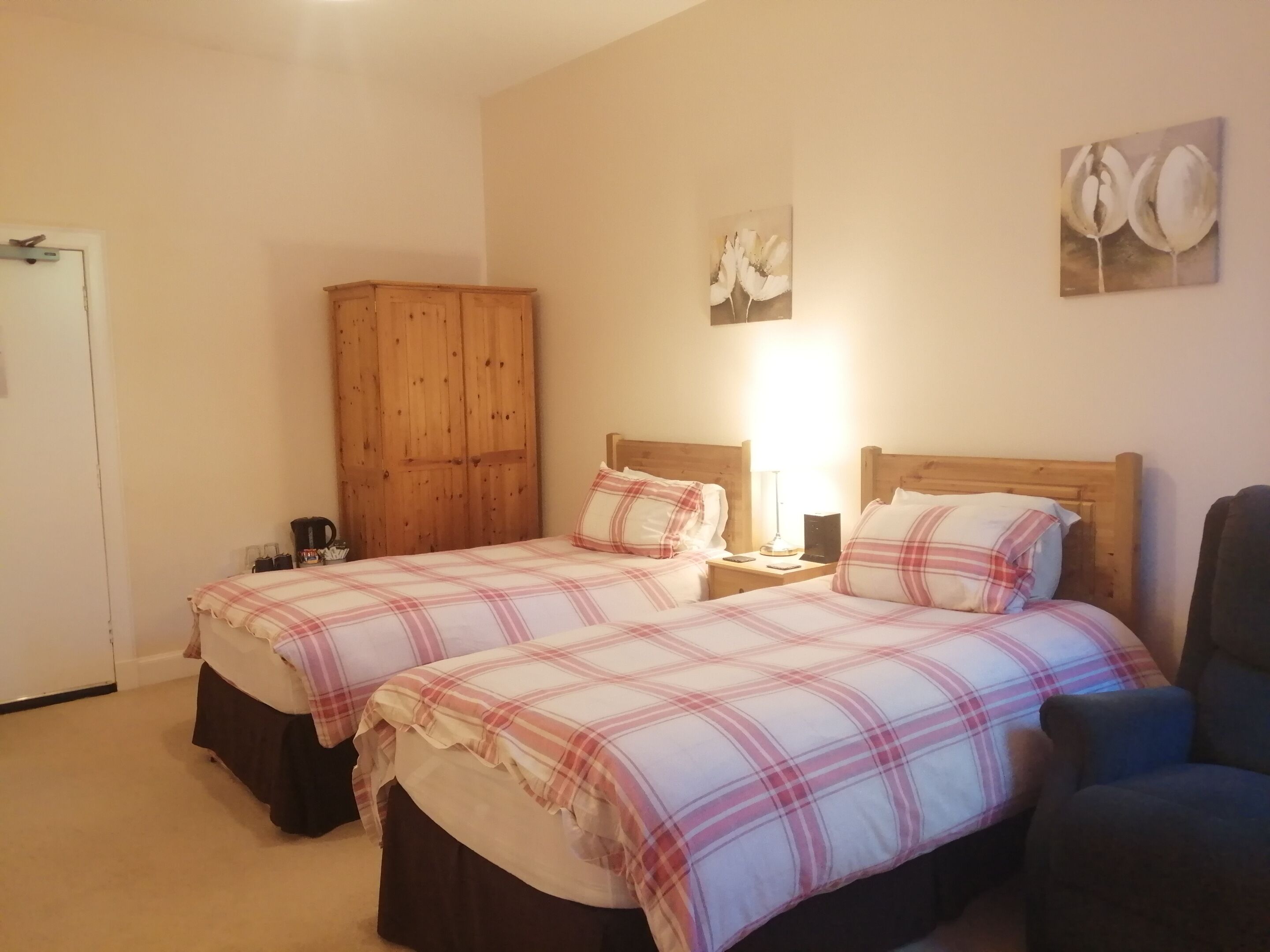 A bedroom with two beds, a wooden wardrobe, a nightstand with a lamp, and a wall art piece.