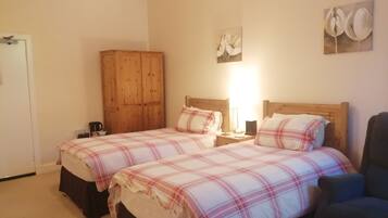 A bedroom with two beds, a wooden wardrobe, a nightstand with a lamp, and a wall art piece.