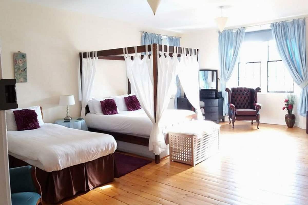 Une chambre spacieuse avec deux lits, un coin salon et une grande fenêtre avec des rideaux.