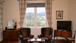 A living room with two leather armchairs, a wooden coffee table, a television on a wooden cabinet, and a window with curtains. - Cuil an Daraich Guest House (Pitlochry)