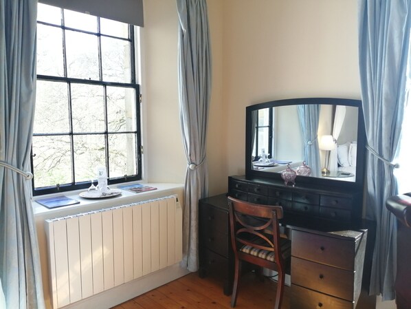 A room with a large window, a radiator, a desk with a mirror, and a chair.