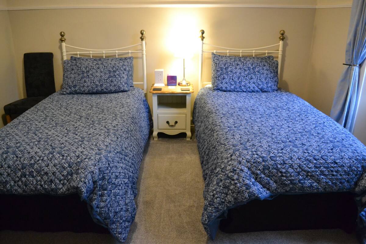 Ein Doppelzimmer mit zwei Betten, einem Nachttisch mit Lampe und einem Sessel.