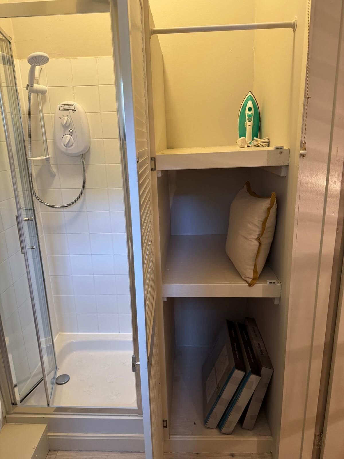 Une salle de bain avec une douche à parois de verre, des toilettes blanches et une étagère sur laquelle se trouvent une serviette et une bouteille verte.