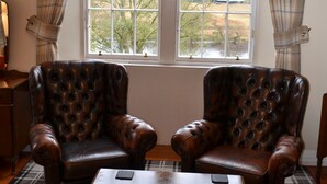 A room with two leather armchairs, a plaid rug, a wooden coffee table, and a window with curtains. - Cuil an Daraich Guest House (Pitlochry)