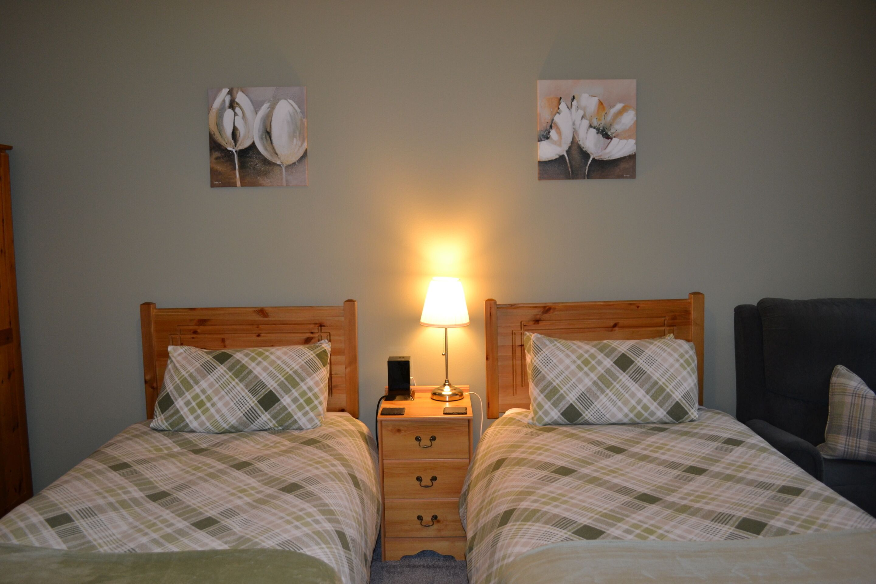 Een tweepersoonsbed met een houten hoofdbord, een nachtkastje met een lamp en twee aan de muur hangende schilderijen.