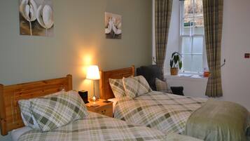 A bedroom with two beds, a bedside table with a lamp, a window with curtains, and wall art.