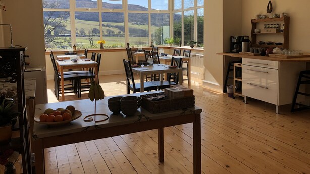 A spacious kitchen with large windows, a dining area with wooden furniture, and a view of hills. - Cuil an Daraich Guest House (Pitlochry)
