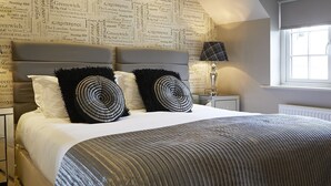 A bedroom with a large bed, a headboard with a printed map, two black and white patterned pillows, a bedside table with a lamp, and a window with daylight. - Five Star Stays (Scarborough)