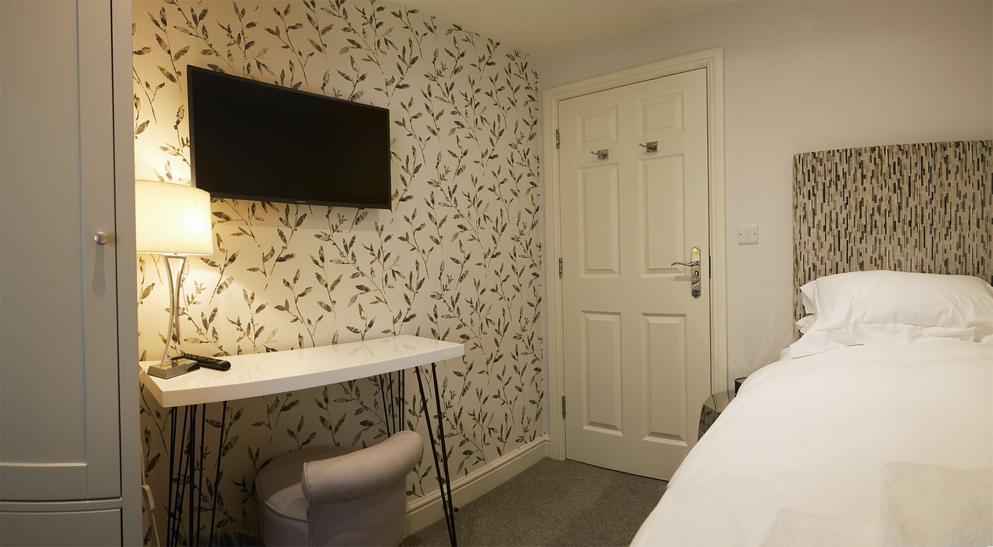 Una habitación de hotel con una cama, un escritorio con lámpara, un televisor y una puerta.
