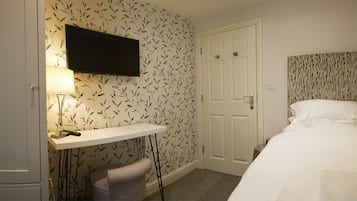 Una habitación de hotel con una cama, un escritorio con lámpara, un televisor y una puerta.