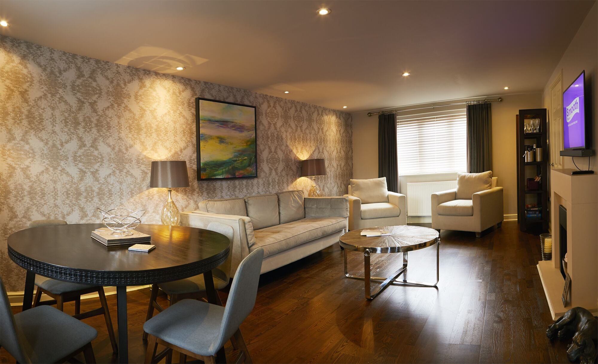 A modern living room with a sofa, two armchairs, a dining table with chairs, a coffee table, and a television.