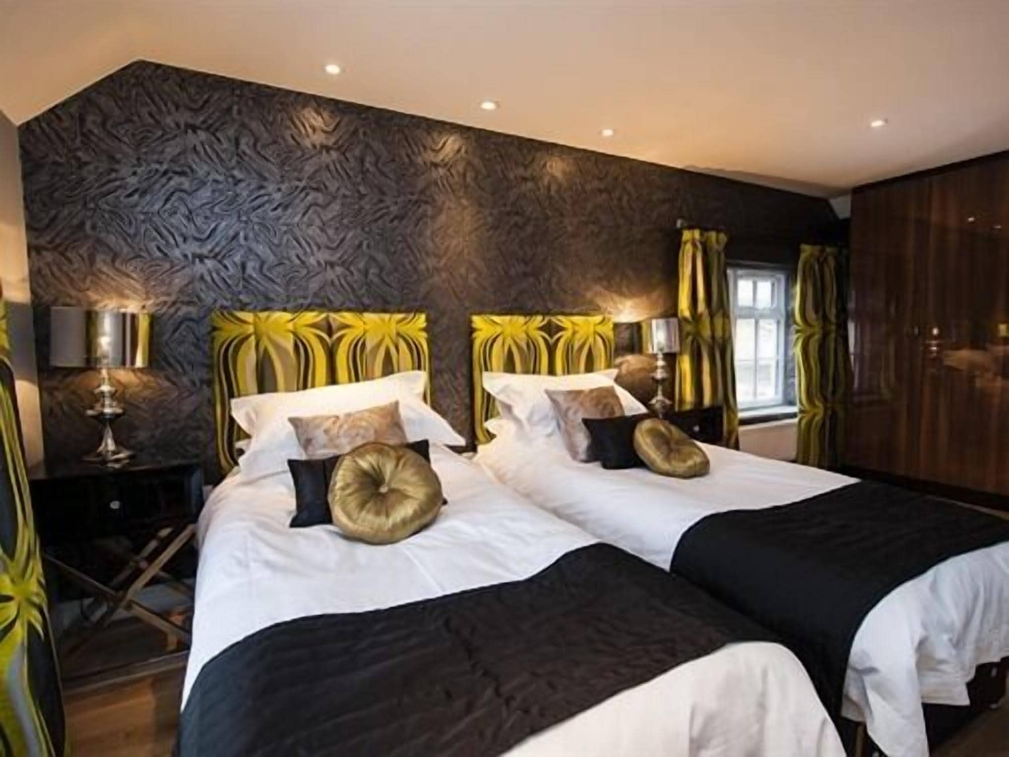 A double bed with a black and white bedspread, two gold accent pillows, and a textured wall behind.
