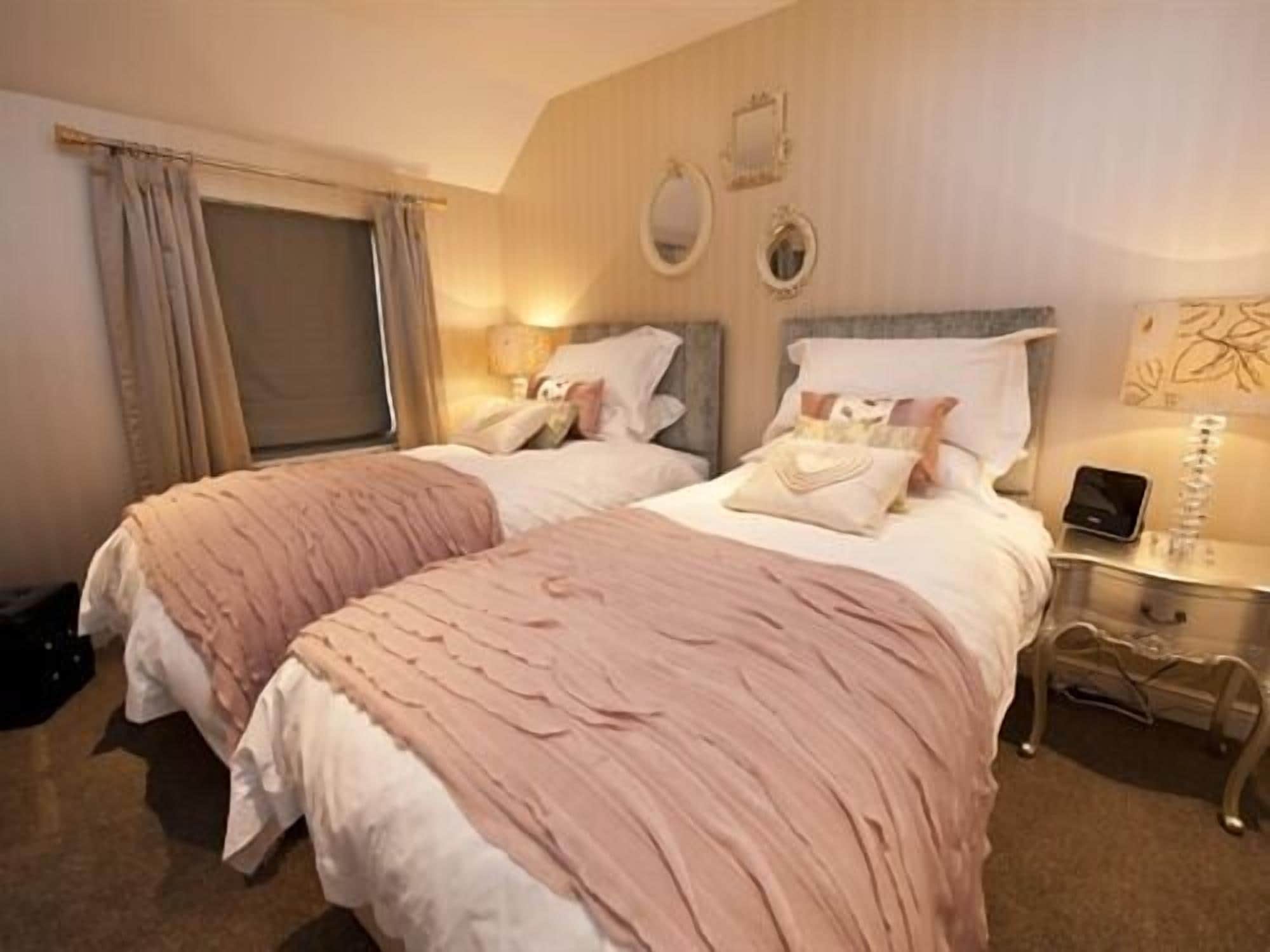 A double bed with a pink and white duvet, a bedside table with a lamp, and a wall-mounted mirror.