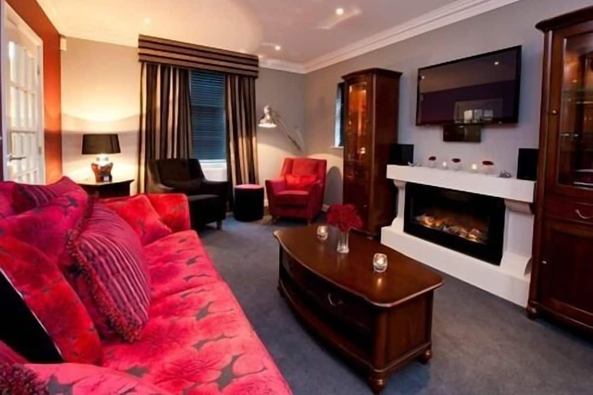 Een woonkamer met een rode bank, een open haard en een aan de muur bevestigde televisie.