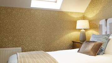 A bedroom with a skylight, patterned wallpaper, a bed with a striped blanket, a bedside lamp, and a nightstand with a lamp.