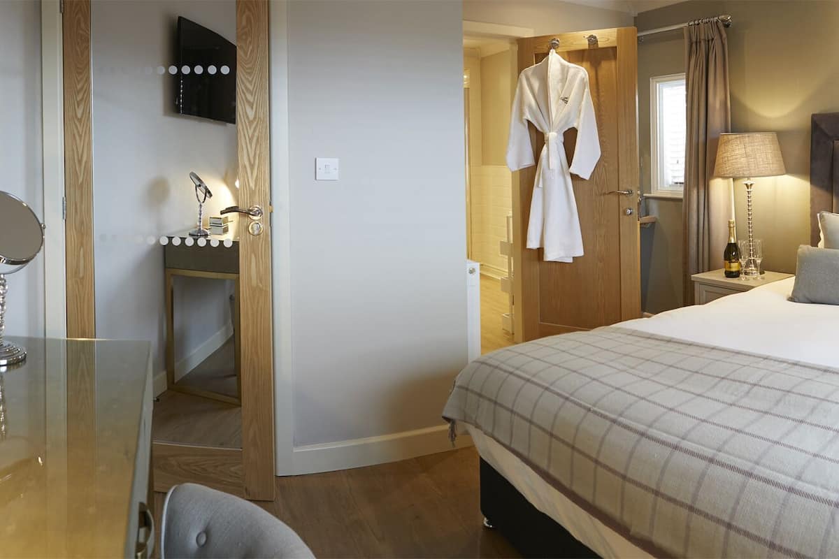 Hotelkamer met een groot bed, een kaptafel met spiegel en verlichting, een badjas hangend aan de deur en een nachtkastje met lamp.
